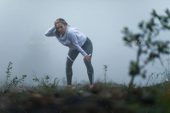 Young female runner feeling exhausted after jogging during foggy weather.
