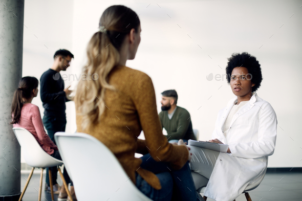 Black female counselor talking to a woman during group therapy at medical center.