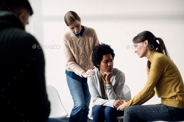 African American woman being consoled by her support group during a therapy.