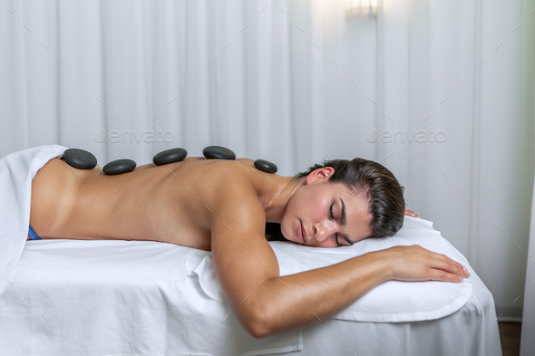 Side view of a young woman lying face down in a massage table with spa stones on her back