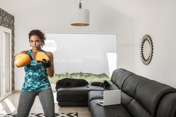 Serious ethnic sportswoman in boxing gloves training at home