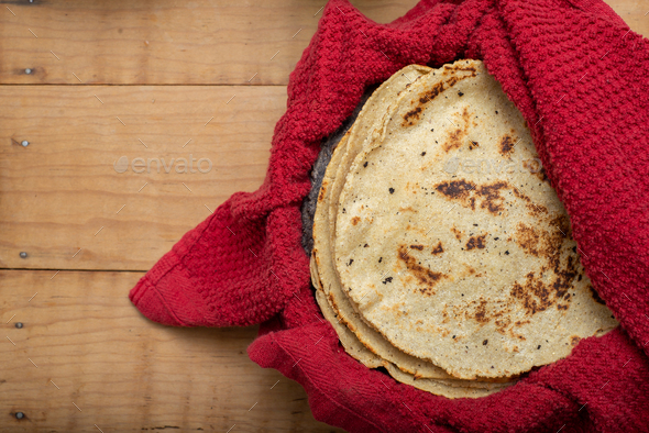 Corn tortillas wrapped in a red cloth on wooden table.