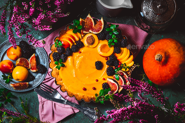 Traditional American pumpkin pie decorated with peaches, blackberries and figs on a green background