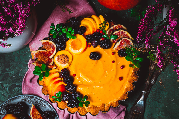 Traditional American pumpkin pie decorated with peaches, blackberries and figs on a green background