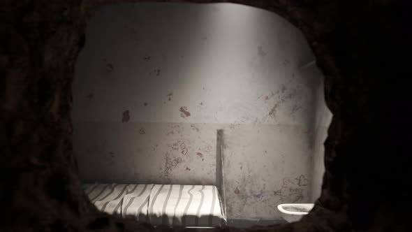 Animation of single old grunge locked prison cell with a hole in the wall. alt