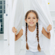 Happy European girl with two plaits, poses near clothes horse between white drying linen - PhotoDune Item for Sale
