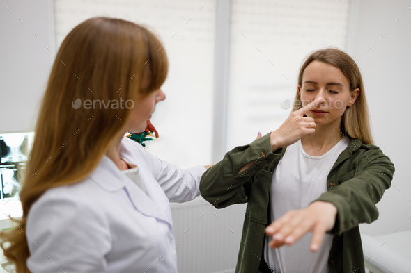 Woman with closed eyes touch nose with fingertip during physical examination.