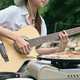 Happy young woman playing guitar on folding chair near the river bank.  - PhotoDune Item for Sale