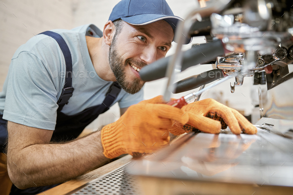 Joyful young man repairing coffee machine in cafe