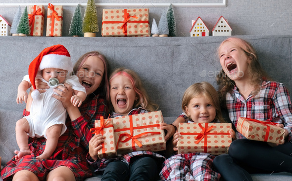  Four sisters with infant little brother sitting on couch with gift boxes.