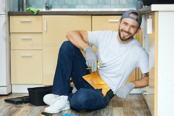 Fix it right. Full length shot of young handyman, plumber wearing tool belt sitting on