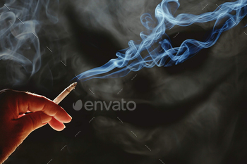 Man's hand holding cigarette with white smoke look like devil face on dark background