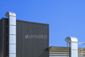Two air ventilation ducts outside of modern industrial building against blue clear sky background