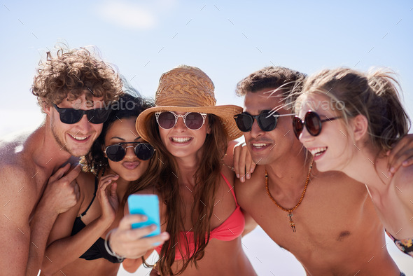 Bringing together a group of best friends. Shot of a group of friends taking selfies on the beach.