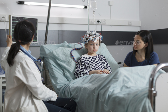 Expert pediatrician monitoring hospitalized girl brain condition using EEG headset