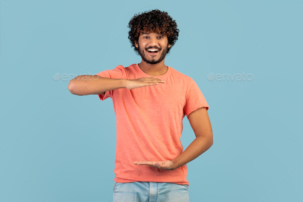 Cheerful handsome indian guy showing something invisible in his hands - Stock Photo - Images