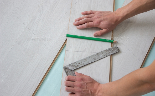 Workers\' hands install a wooden laminate floor.