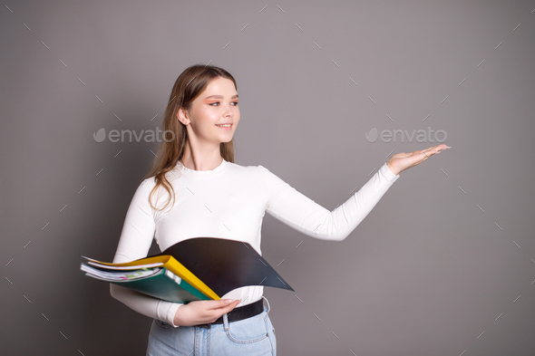 A cute student girl holds notebooks for notes and points to the side with her hand