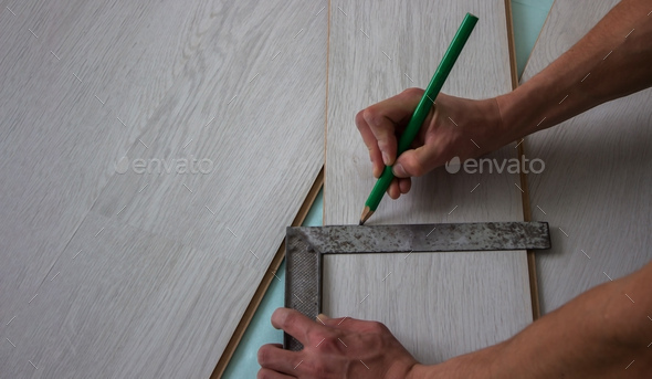 Workers' hands install a wooden laminate floor.