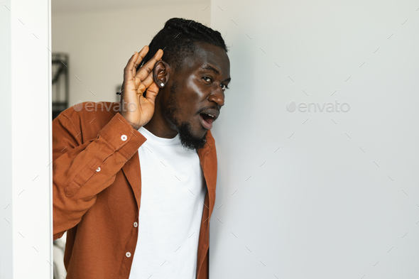 Black man listening holding hand near ear, standing in opened door having problem with soundproof at