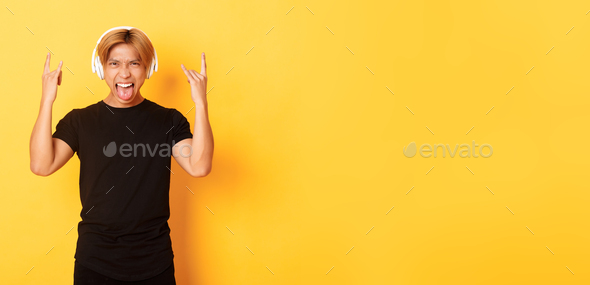 Sassy handsome asian guy likes heavy metal, listening hard rock music, showing rock-n-roll gesture