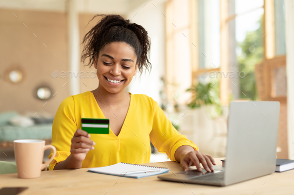 Making financial transaction. Excited black lady holding credit card and using personal computer