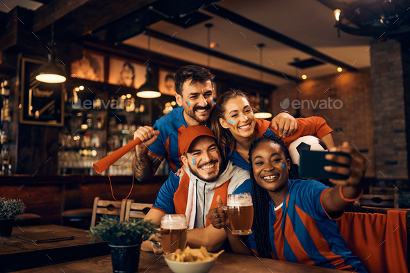 Cheerful group of soccer fans taking selfie while having fun in pub.