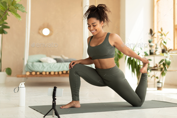 African american fitness blogger shooting online video tutorials, showing legs quad stretching