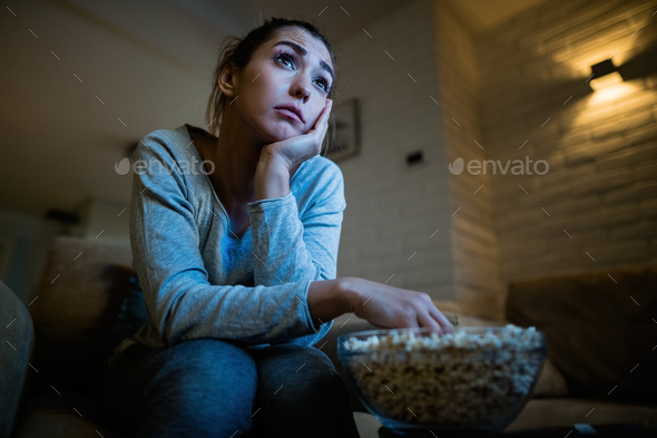 Below view of woman eating popcorn while watching sad movie at home.