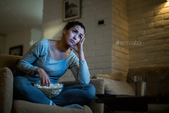 Young woman watching sad movie and eating popcorn in the evening at home.