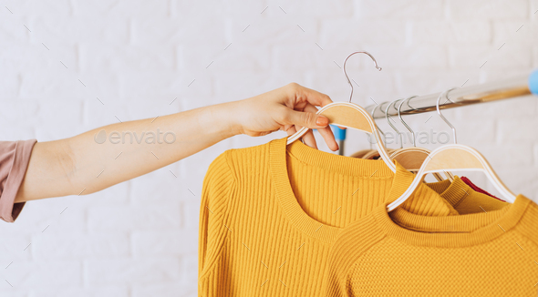 Woman\'s hand removes yellow knitted jacket on wooden hanger from an iron rack rale