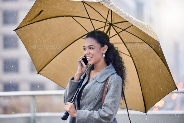 Im caught in the rain. Shot of a young woman holding an umbrella while on a call in the rain.