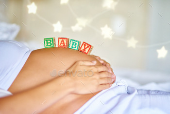 Coming soon. Closeup shot of a pregnant woman lying down with wooden baby blocks on her belly.