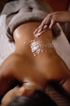 Lightly salted...Shot of a young woman enjoying a salt exfoliation treatment at a spa.