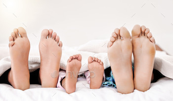 Earth descending, heaving ascending. Shot of a familys bare feet while sleeping in bed together.
