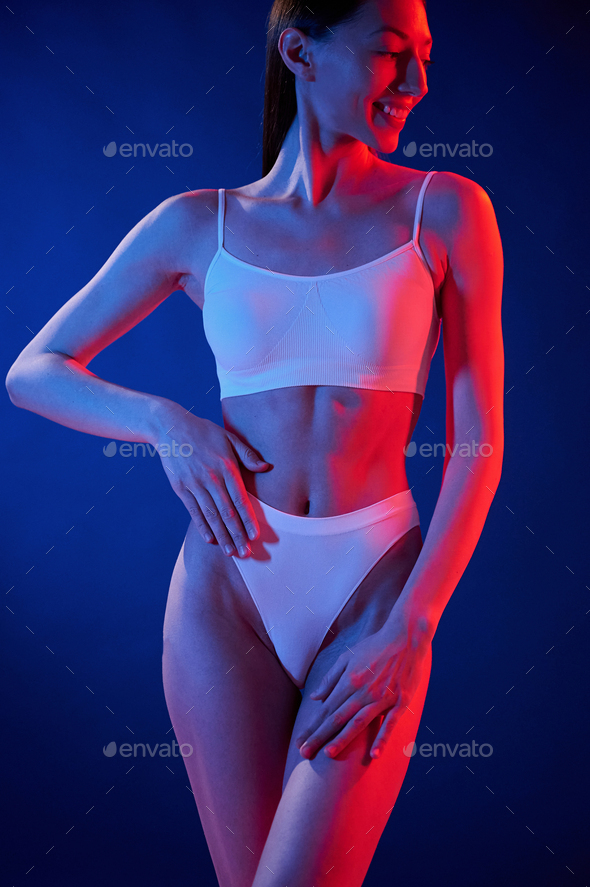 Slim body type. Young woman in underwear is in the studio with neon lights  Stock Photo by mstandret