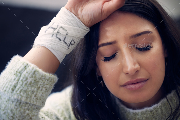 Shot of a young woman with bandages wrapped around her wrists showing help written on them