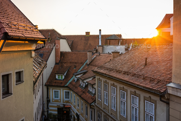 Sun setting over rooftops with red tiles in a city with old houses