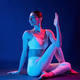 Sitting on the floor. Young woman in sportive clothes is in the studio with neon lights - PhotoDune Item for Sale