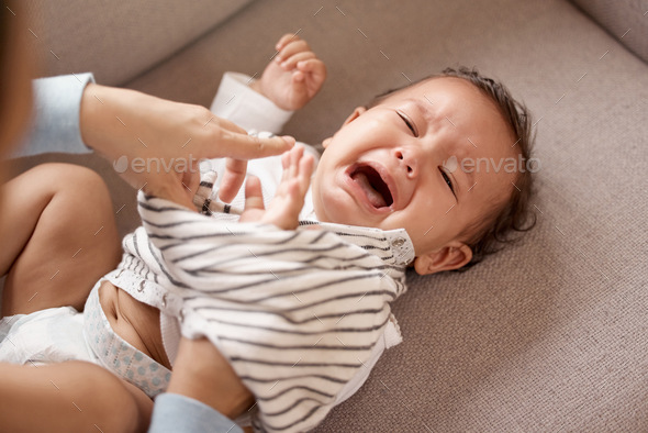 Shot of a young baby girl crying while her mother changes her clothes at home
