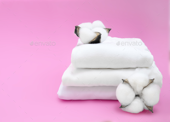 Cotton plant and white folded fabric on pink background. Cotton clothes fabric concept. Minimalism a