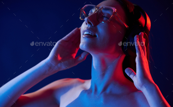 Feel the music. In headphones. Portrait of young woman that is indoors in neon lighting - Stock Photo - Images