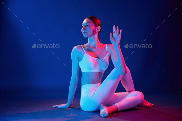 Sitting on the floor. Young woman in sportive clothes is in the studio with neon lights - Stock Photo - Images