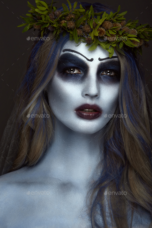 Portrait of a horrible scary Corpse Bride in wreath with dead flowers, halloween makeup