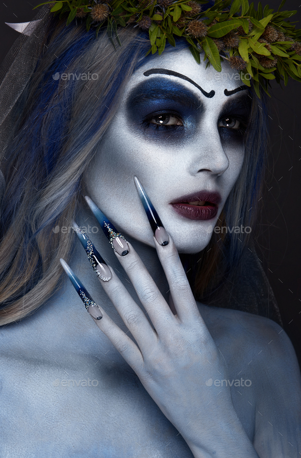 Portrait of a horrible scary Corpse Bride in wreath with dead flowers, halloween long manicure
