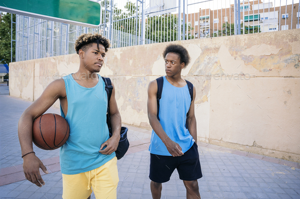 Two athletic young men going to the basketball court holding bags and a basketball