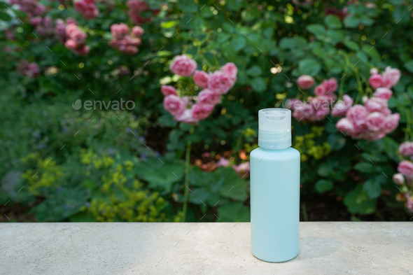 blue skin tonic or lotion in a plastic cosmetic bottle with rose flowers nature background