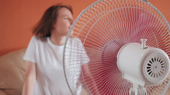 Young Woman Sits in Front of Electric Home Fan Air Stream Blowing Short Hair alt