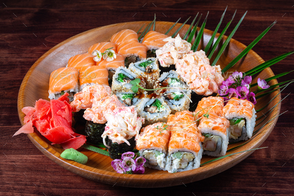 Sushi and rolls with sauce and spices on wooden plate with green leaves - Stock Photo - Images