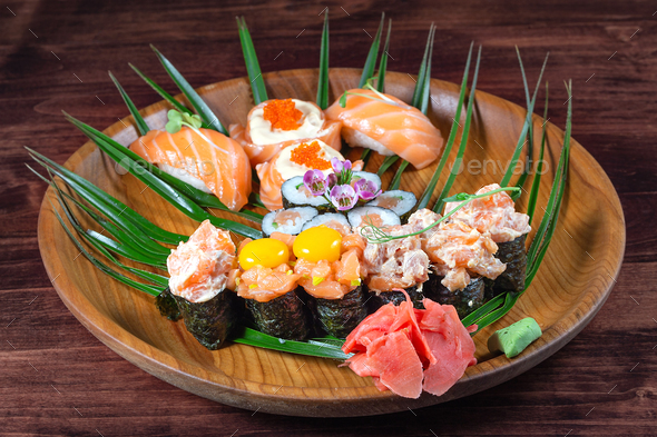 Sushi and rolls with raw quail eggs on wooden plate with green leaves - Stock Photo - Images